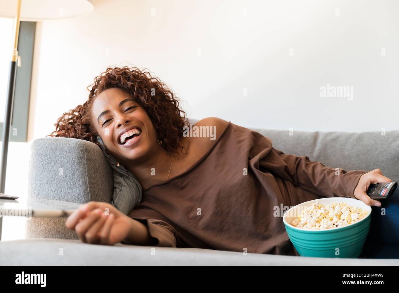 Donna ridente sul divano con telecomando TV e popcorn Foto Stock