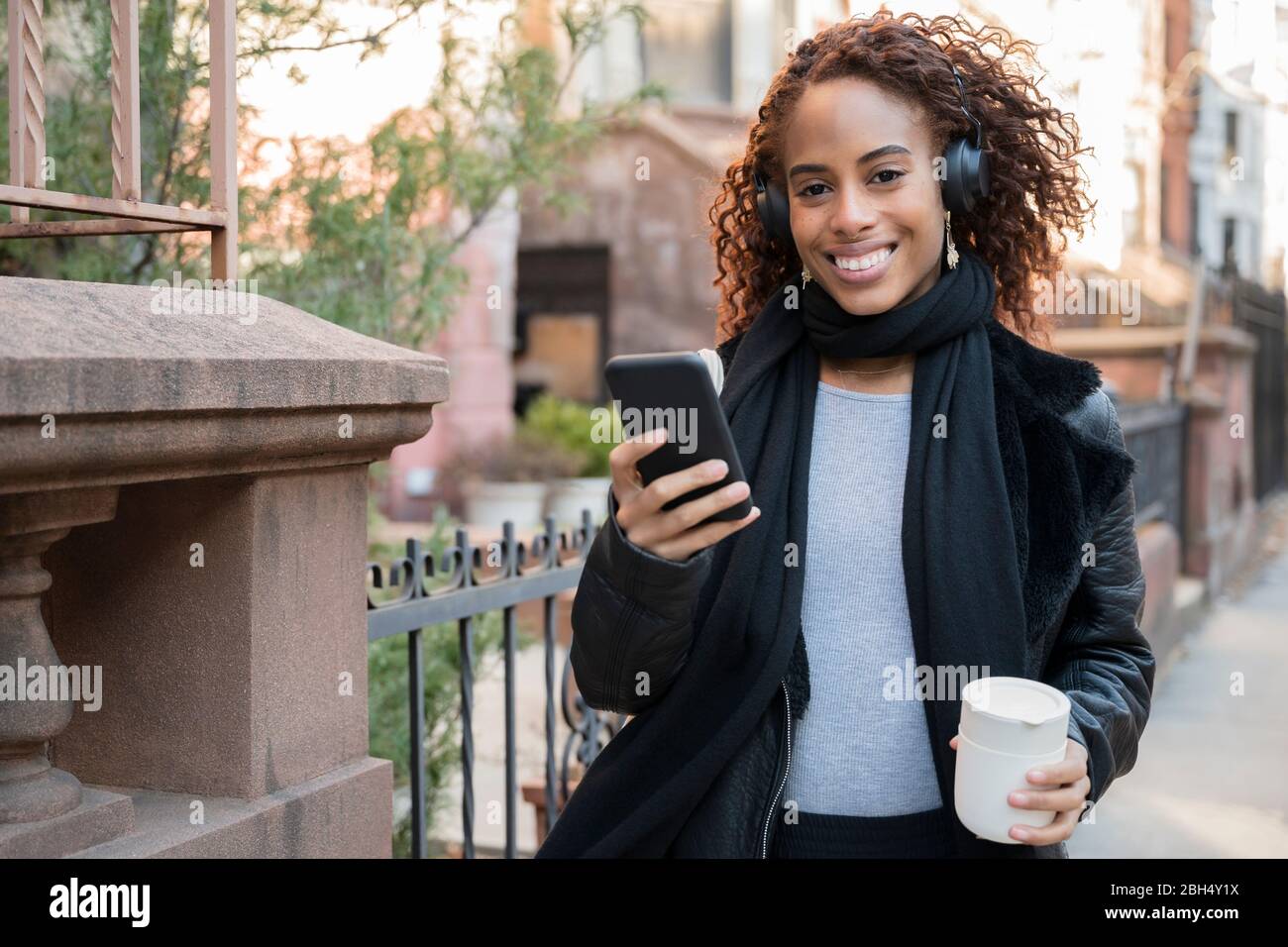Donna sorridente che indossa cuffie con smartphone e coppa Foto Stock