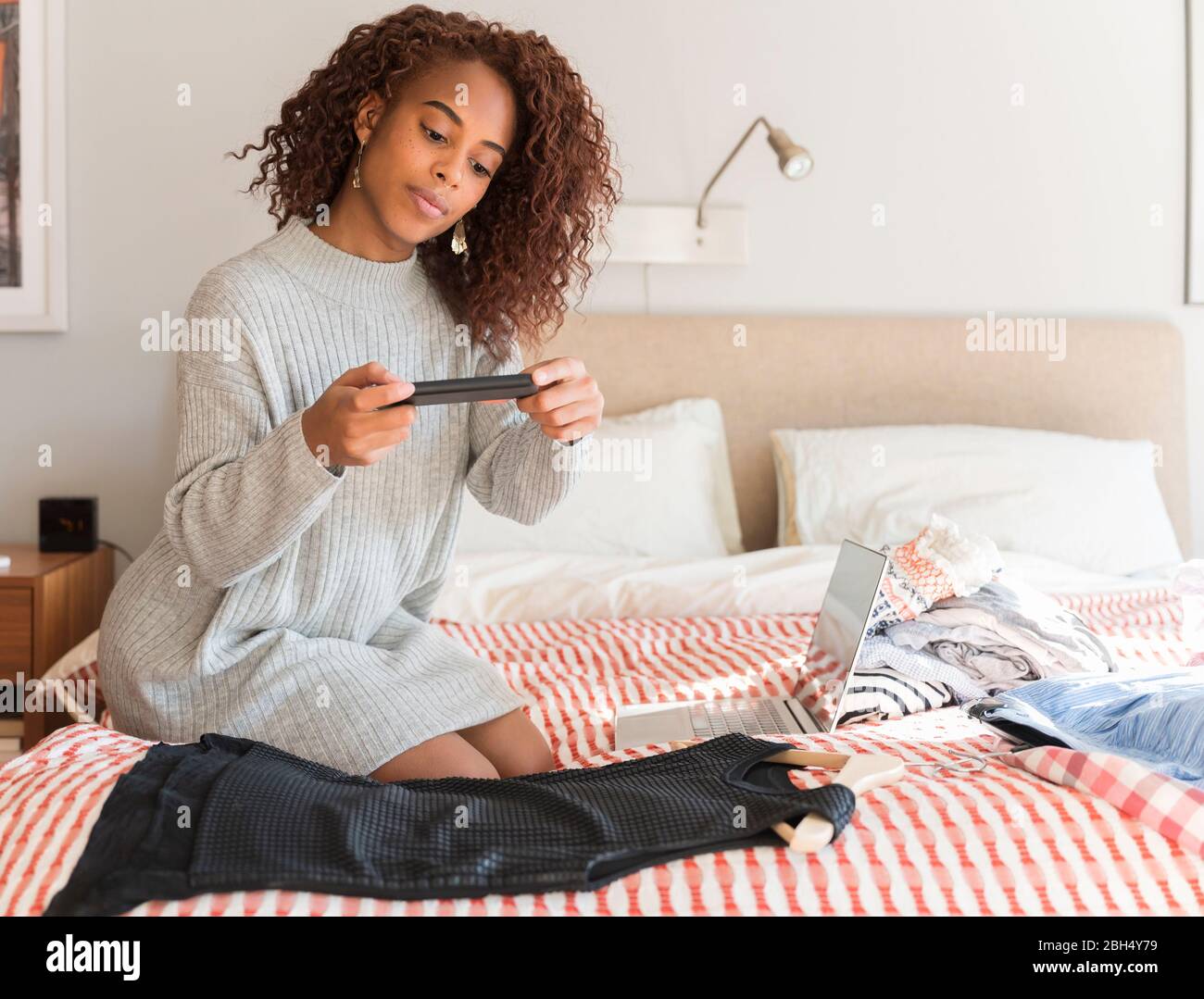 Donna a letto fotografando abiti con smartphone Foto Stock