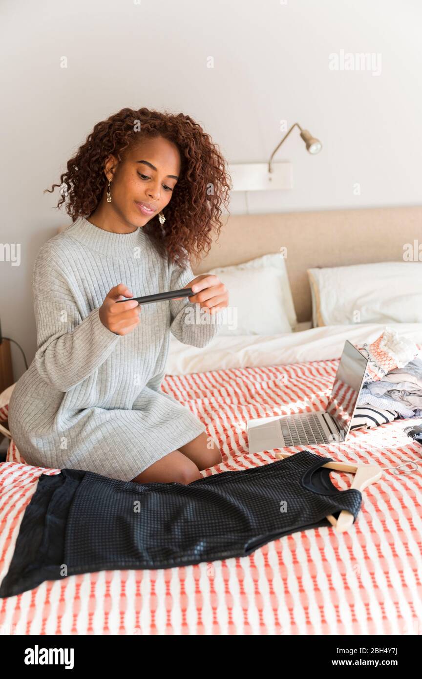 Donna a letto fotografando abiti con smartphone Foto Stock