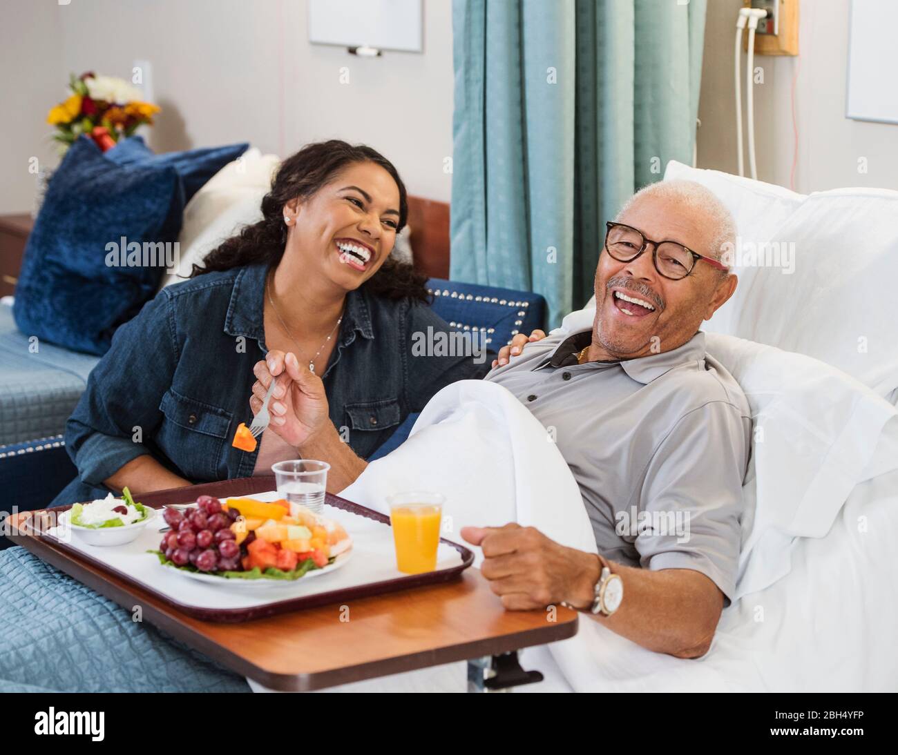 Donna ridente seduta dall'uomo anziano che mangia frutta a letto Foto Stock