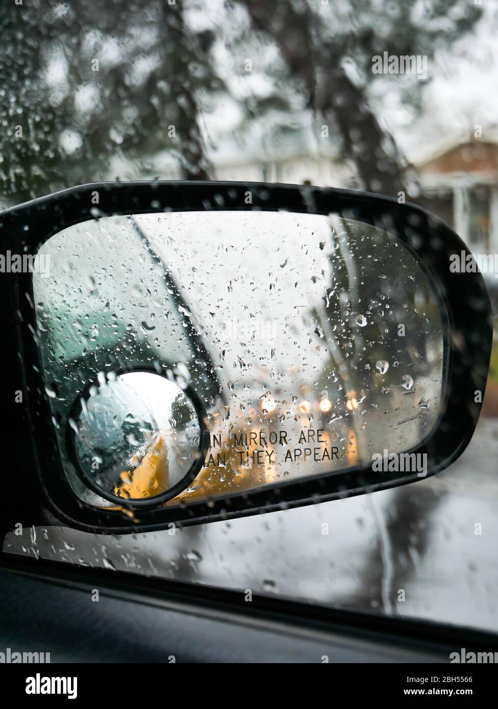 specchietto per auto sotto la pioggia con gocce di pioggia sullo specchio giallo nero bagnato Foto Stock