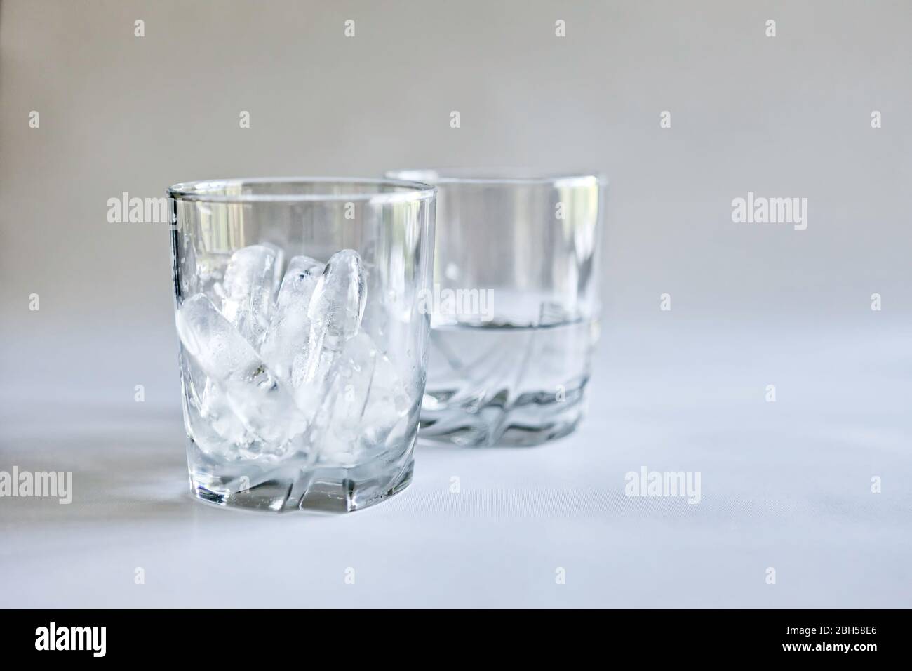 Vista di profilo di bicchieri di ghiaccio e acqua (ghiaccio fuso) in bicchieri trasparenti su sfondo neutro, concetti di tempo e cambiamento, colore Foto Stock