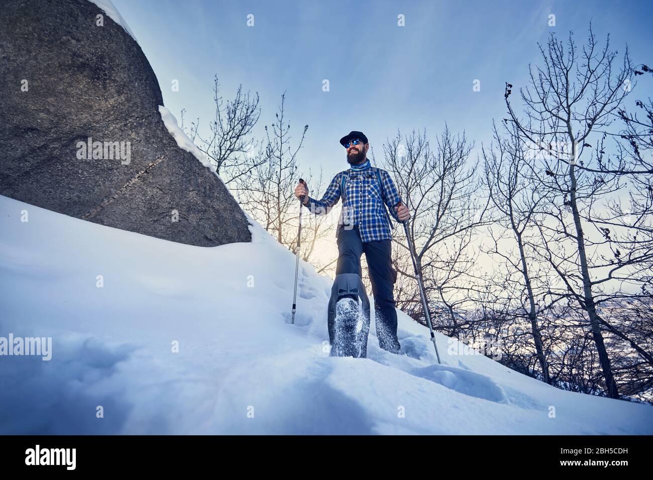 Felice escursionista con la barba in racchette da neve in inverno foresta a cielo blu sullo sfondo Foto Stock