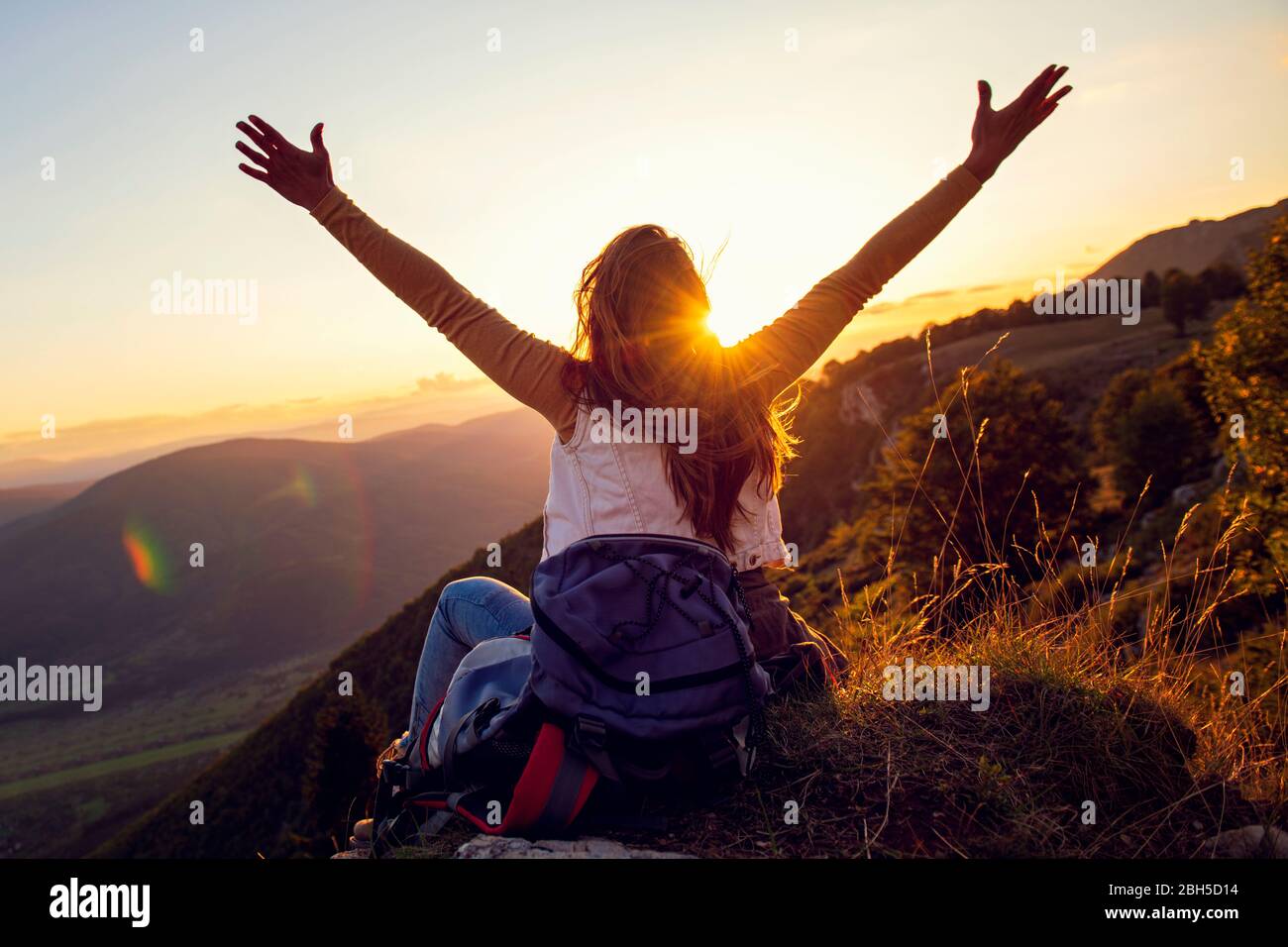 Giovane donna alzarsi mano su in cima alla montagna e tramonto cielo sfondo astratto. Foto Stock