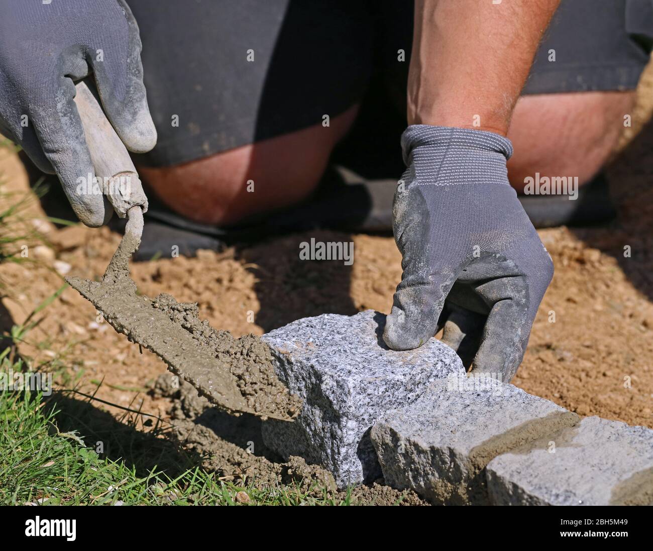 Primo piano di lavoratore con trowel e guanti, posa di un bordo prato blocchi di granito massiccio come parte della limitazione del giardino Foto Stock