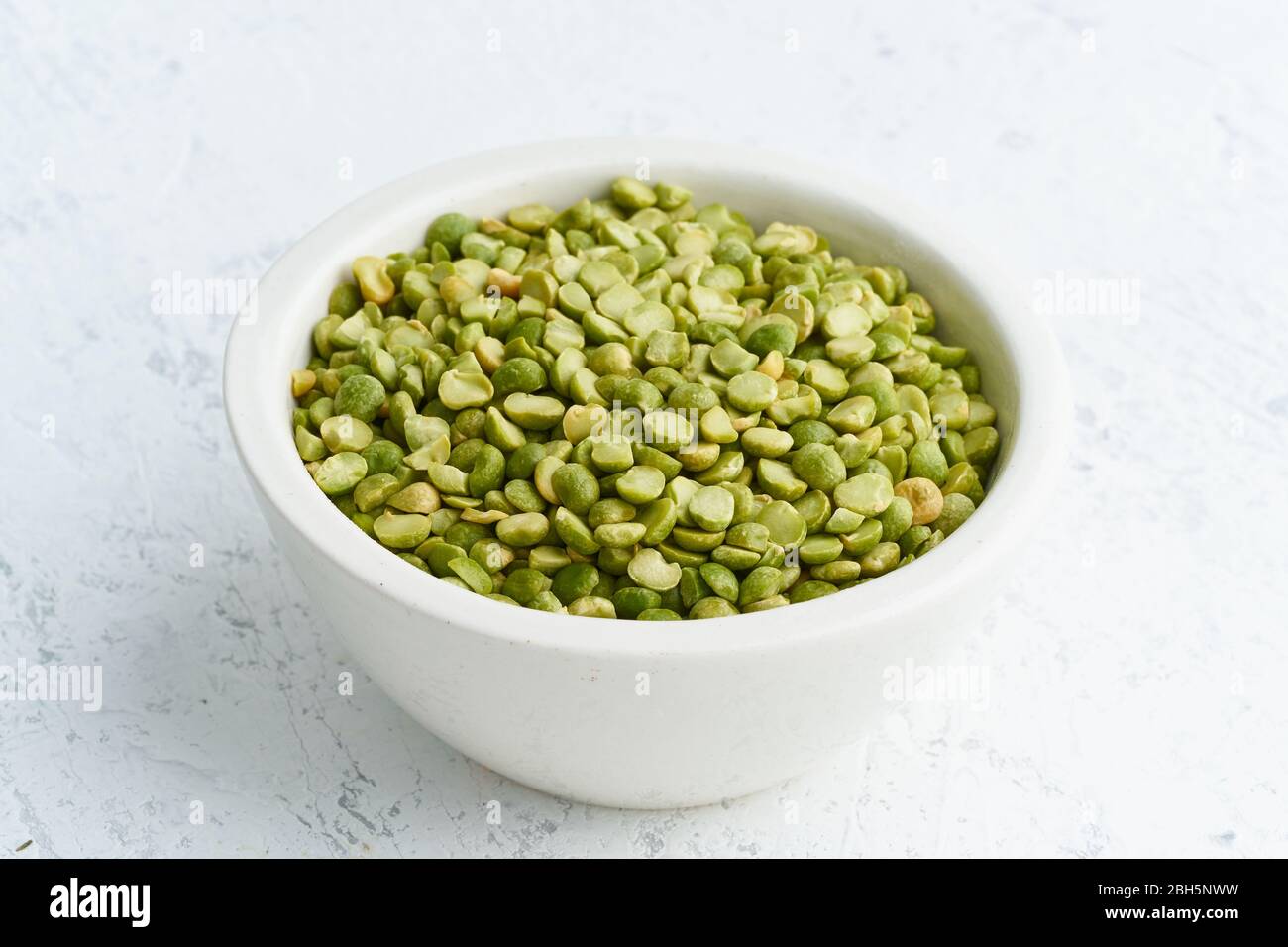 Piselli verdi in ciotola bianca su sfondo bianco. Cereali secchi in tazza, cibo vegano. Vista laterale Foto Stock