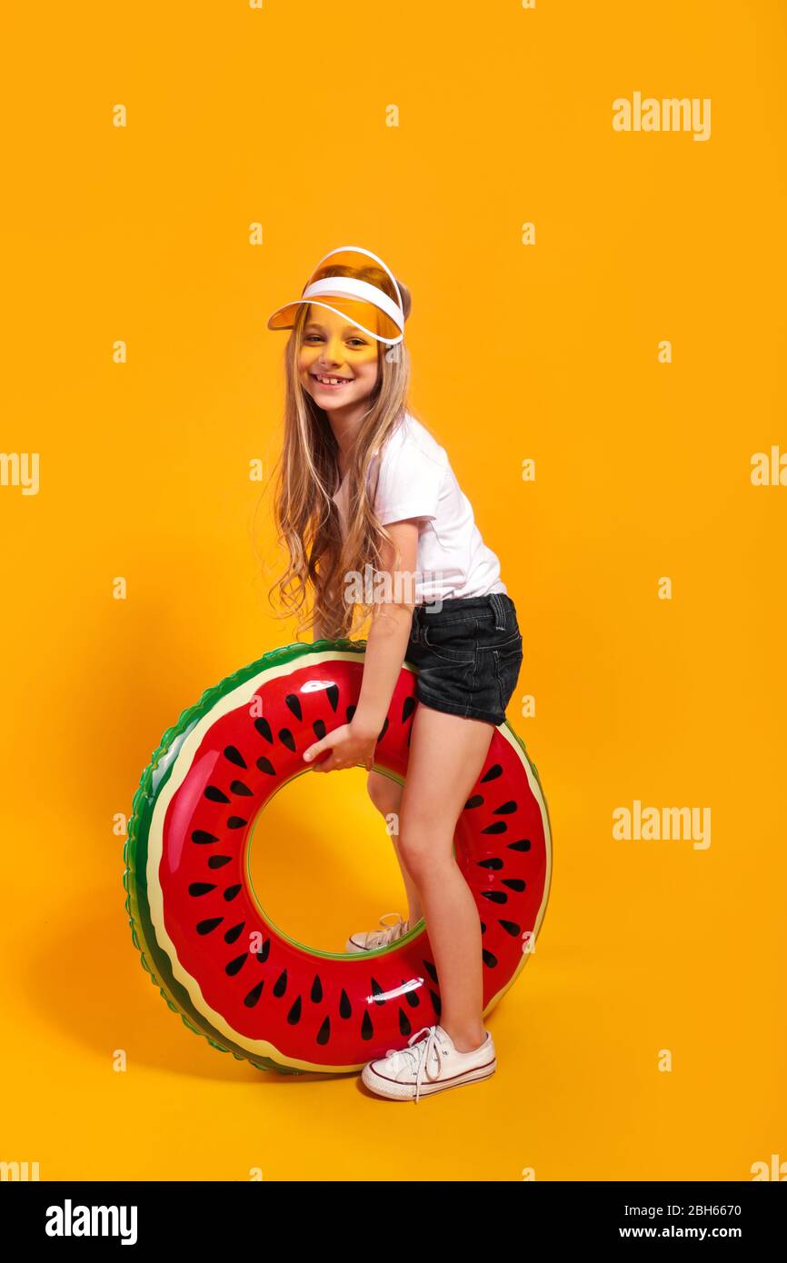 Ragazza allegra bambina in abiti estivi con un anello da nuoto su uno sfondo giallo colorato. Foto Stock