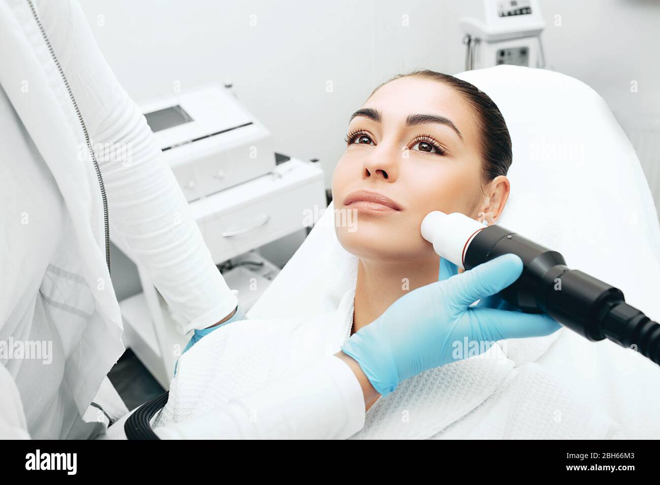 Estetista utilizzando una macchina ad onde acustiche ringiovanisce la pelle del viso di una donna. Ringiovanimento cutaneo indolore Foto Stock