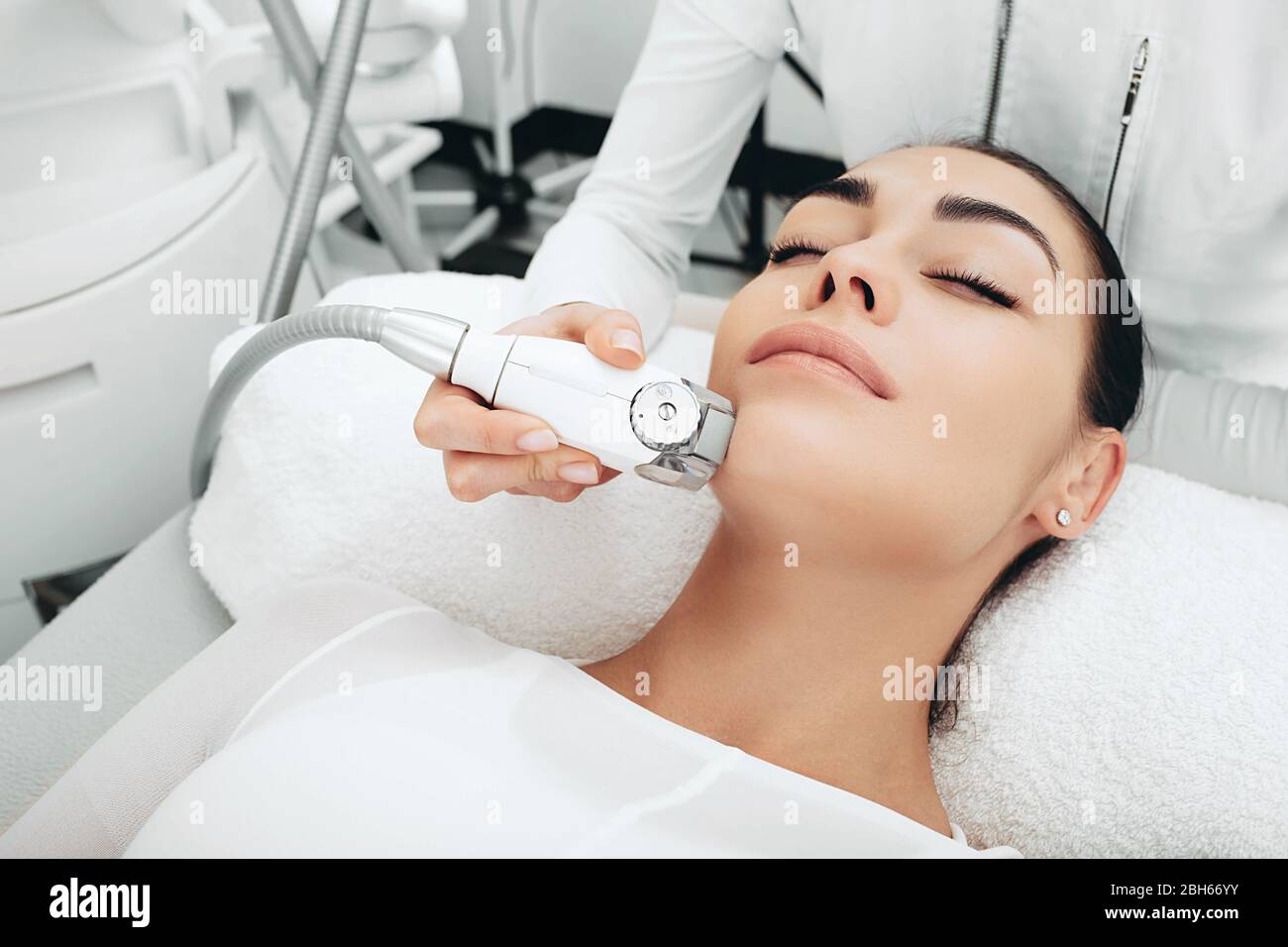 Il cosmetologo che utilizza un apparecchio di massaggio facciale leviga le rughe del viso, leviga il microrelief della pelle. I contorni del viso diventano più chiari Foto Stock