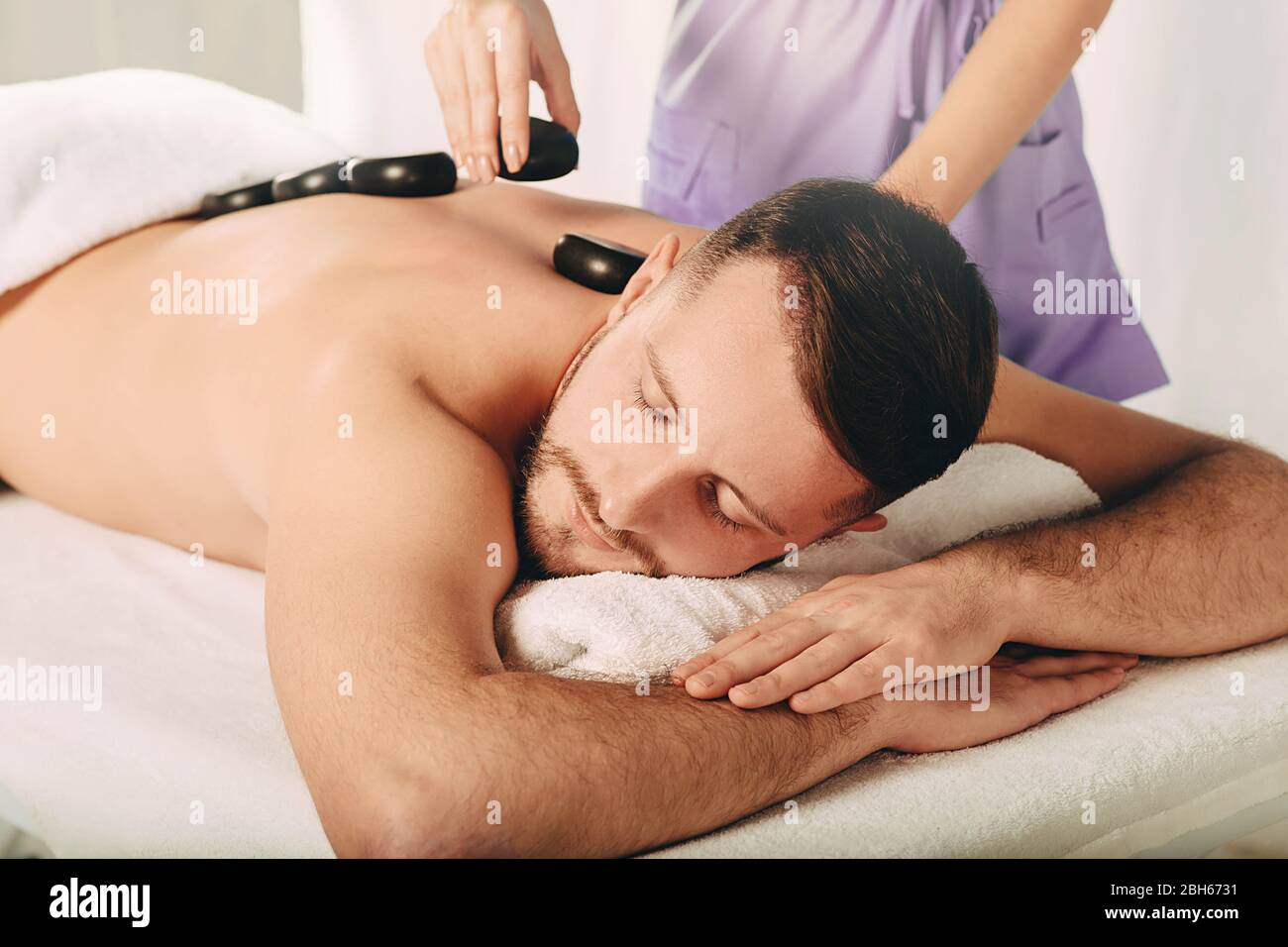 Massaggiatore professionale massaggiante cliente indietro con pietre calde. Terapia alternativa, trattamento con pietre calde Foto Stock