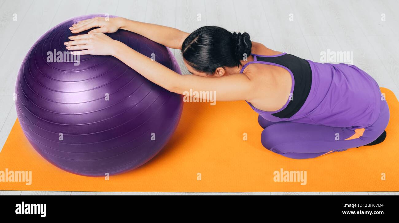 Donna sottile che la allunga indietro usando la sfera dei pilates. Allenati a casa Foto Stock