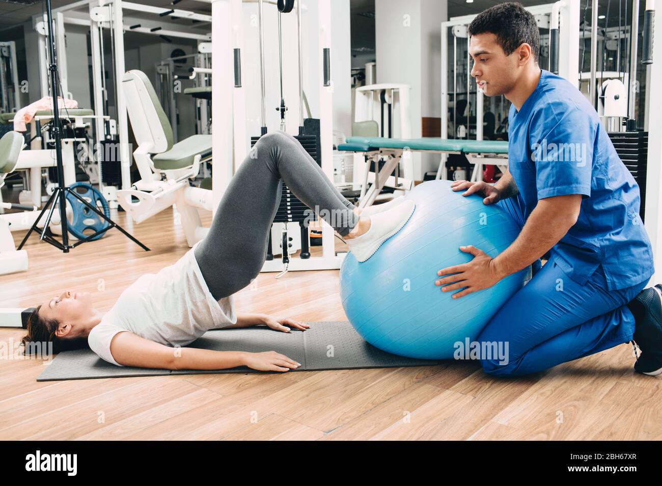 Fisioterapista tiene la sfera di idoneità che aiuta il paziente che fa l'esercitazione posteriore. Ginnastica per la schiena di una donna Foto Stock