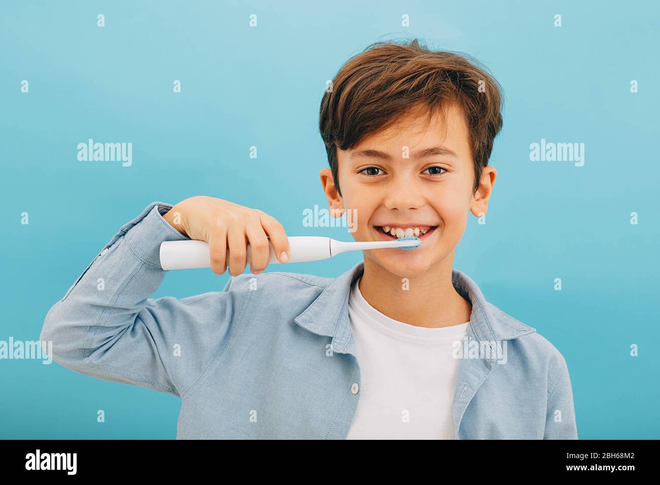 Denti di pulizia del ragazzino di razza mista con spazzolino sonico su sfondo blu. Piastra di rimozione perfetta con spazzolino fresco Foto Stock