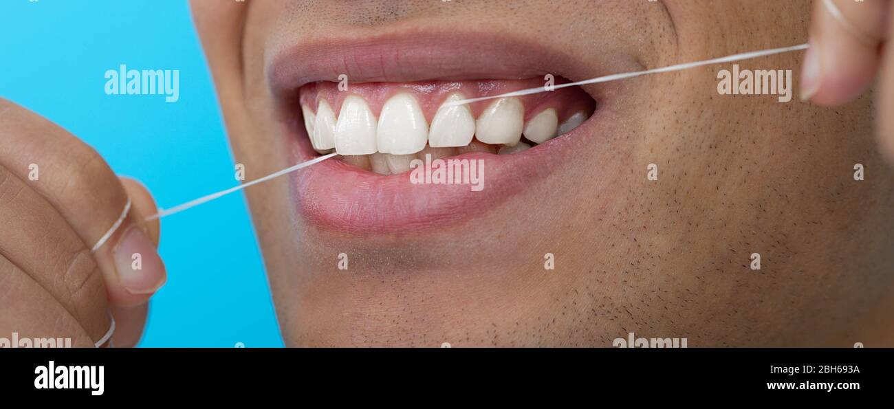 Chiudi la bocca maschile mentre flossi i denti con filo interdentale su sfondo blu. Igiene dentale Foto Stock
