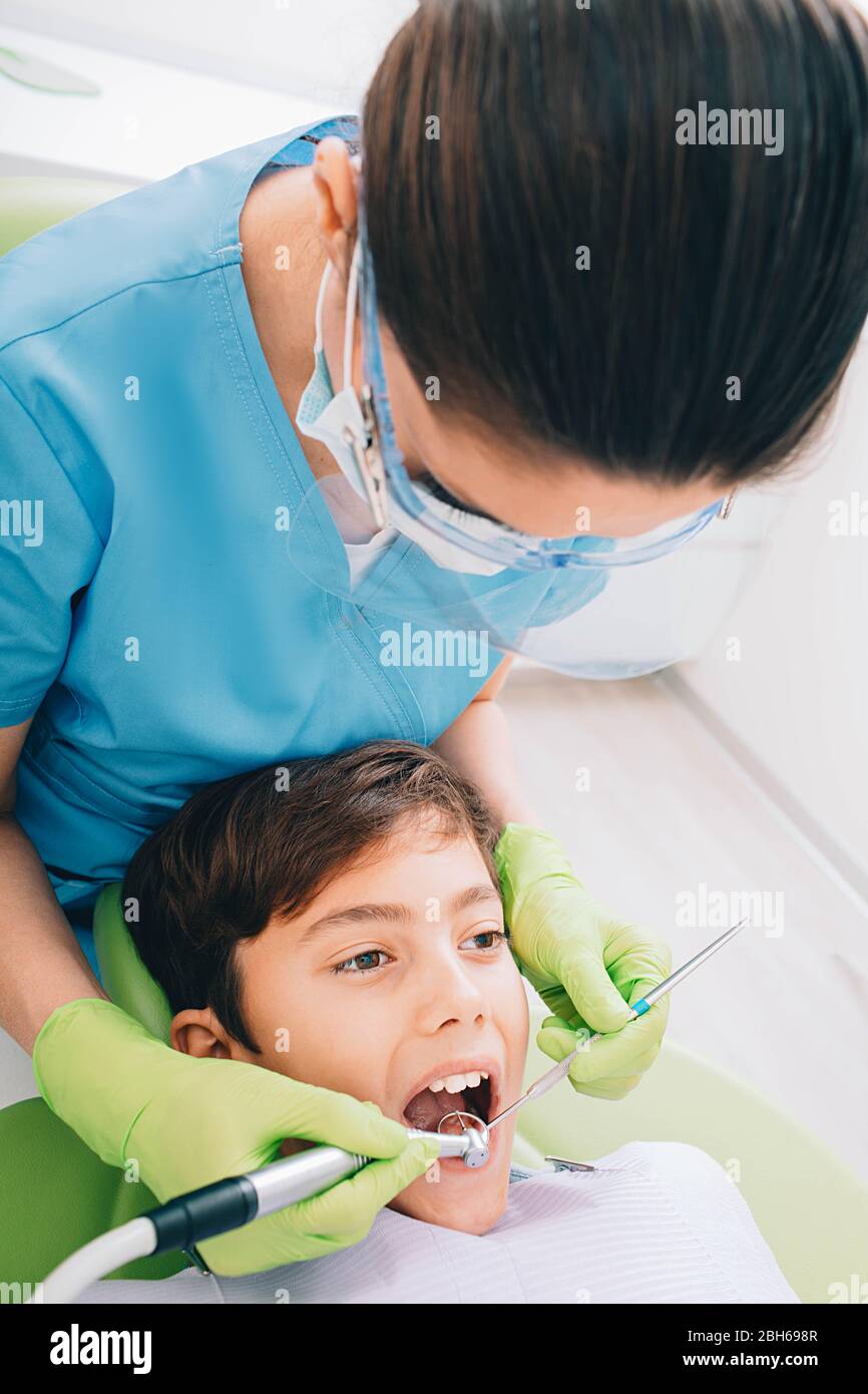 Dentista che fa il trattamento dei denti con dentale trapanare ad un bambino piccolo all'ufficio medico Foto Stock