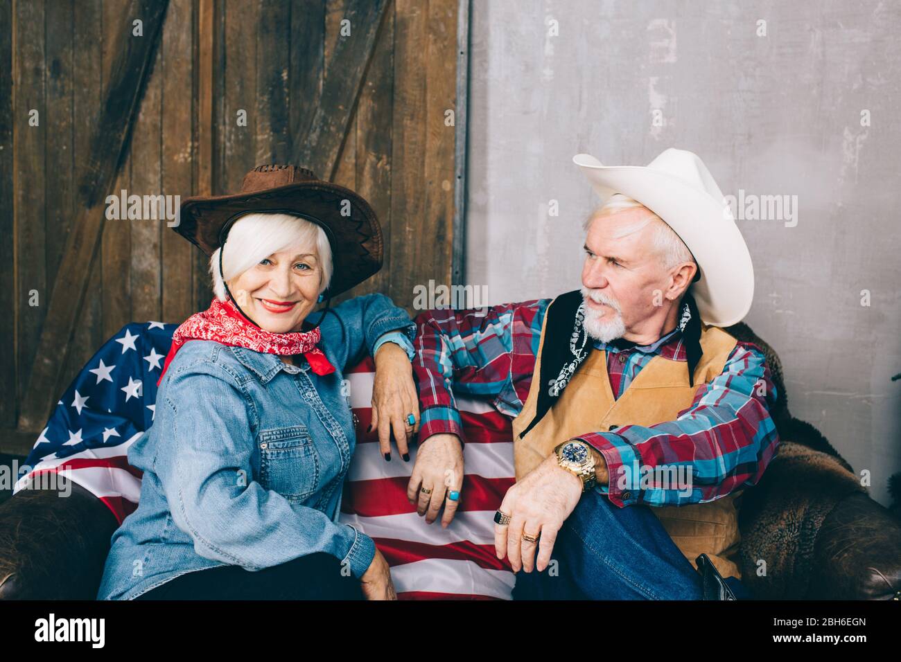 Coppia anziana vestita in stile cowboy, seduta su un divano con bandiera americana. Per celebrare la Giornata dell'Indipendenza in America Foto Stock