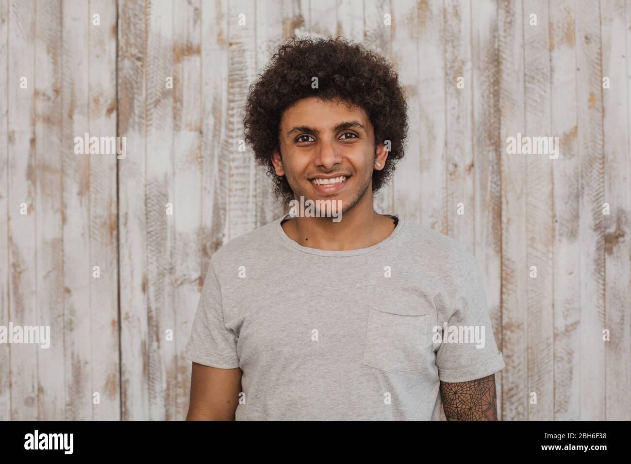 Mulatto con un sorriso perfetto. Ritratto allegro dai capelli ricci uomo guardando la telecamera, mentre in piedi contro il vecchio sfondo di legno Foto Stock