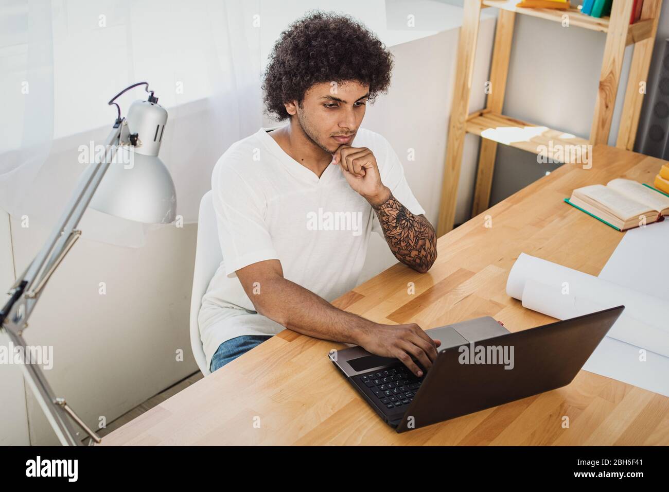 Studio a casa con un notebook. Un uomo attraente si è concentrato guardando il notebook e il pensiero. Foto Stock