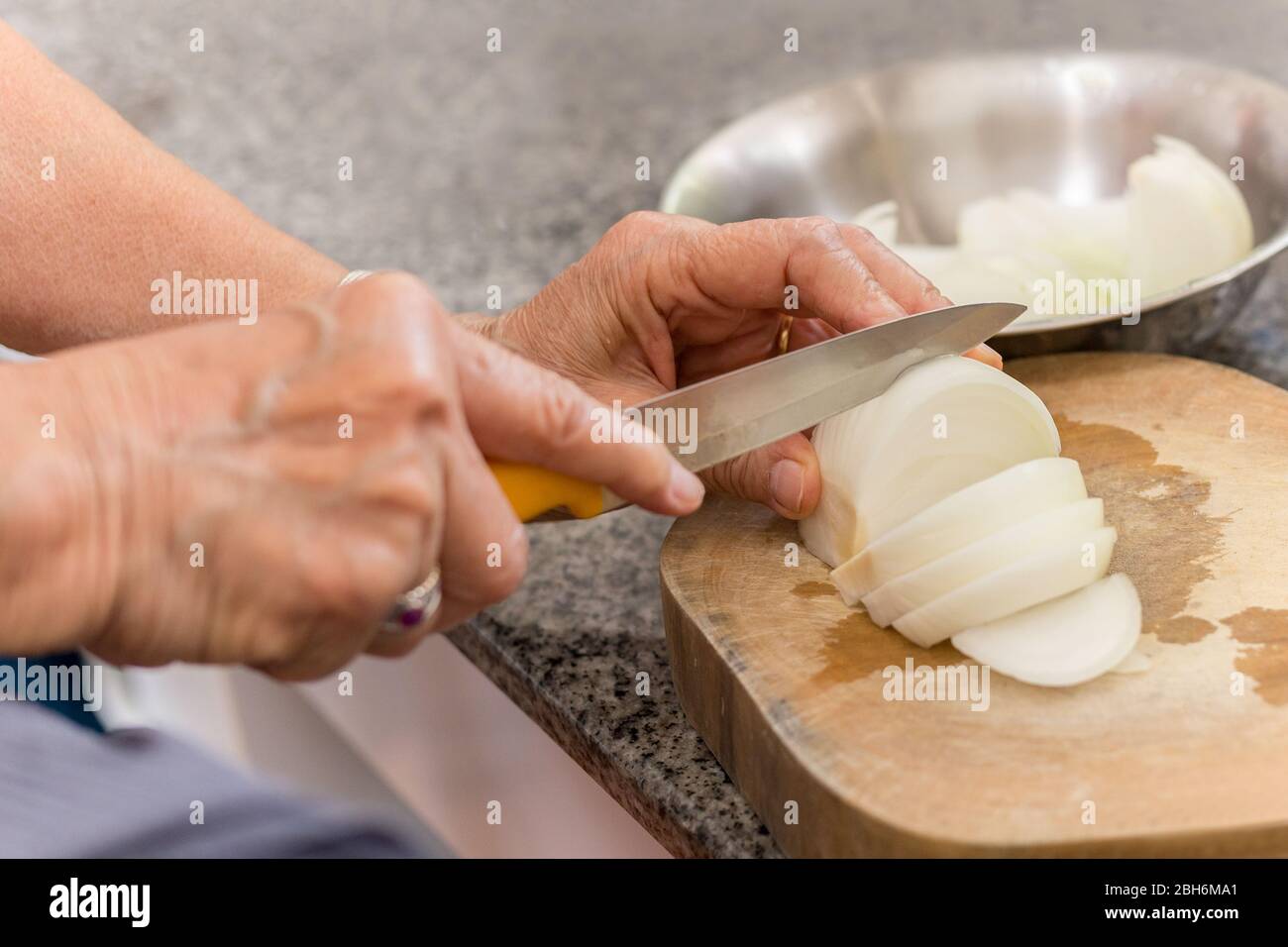 Donna anziana mani tritare la cipolla su un asse di legno in cucina. Foto Stock