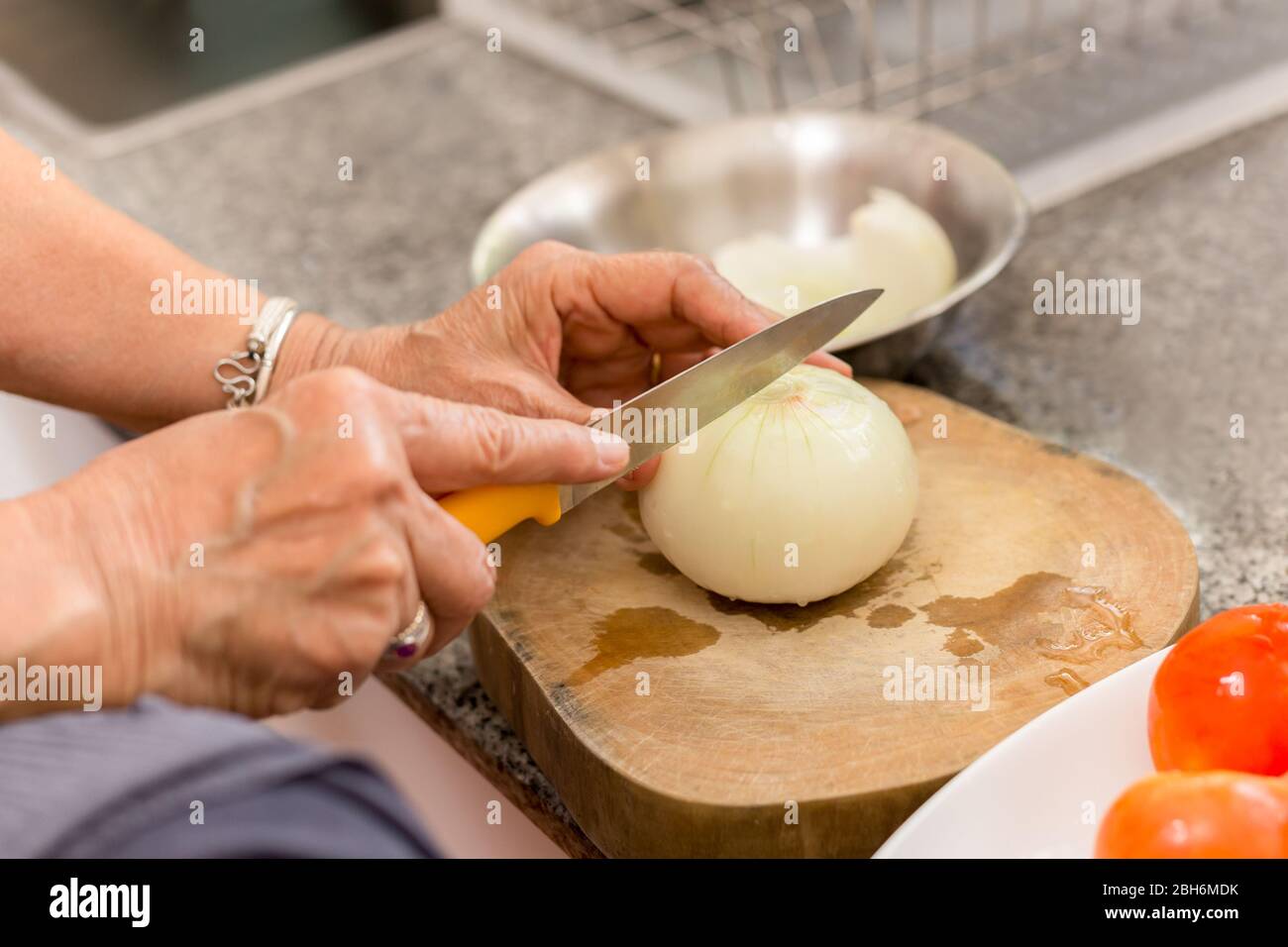 Donna anziana mani tritare la cipolla su un asse di legno in cucina. Foto Stock