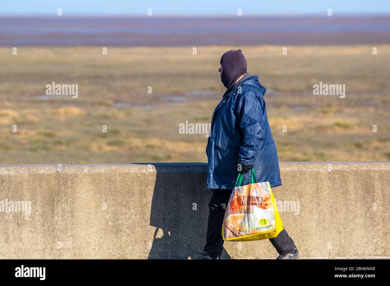 Southport, Merseyside. Meteo Regno Unito. 24 aprile 2020. Uomo che indossa la balaclava e porta con sé una borsa riutilizzabile Morrisons in un'altra luminosa giornata di primavera nel resort, mentre i residenti locali si esercitano sulla passeggiata lungomare. Credit: MediaWorldImages/AlamyLiveNews Foto Stock