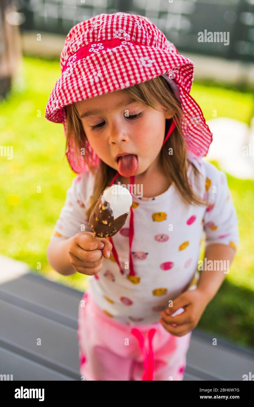 Bambino che mangia gelato su bastone . Bambina in cortile Foto Stock