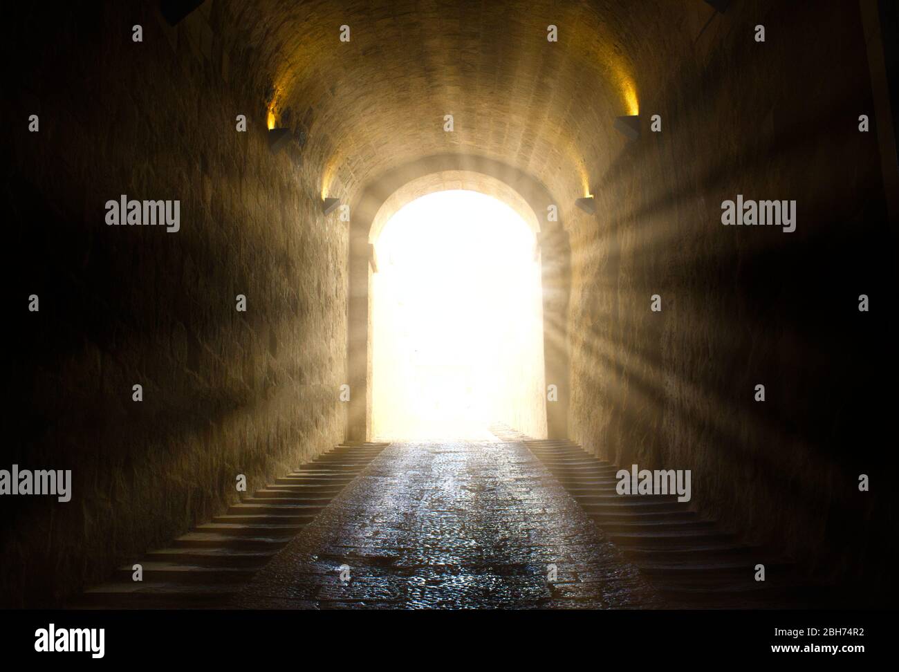 Una luce brillante gialla che si infrange alla fine di un tunnel scuro Foto Stock