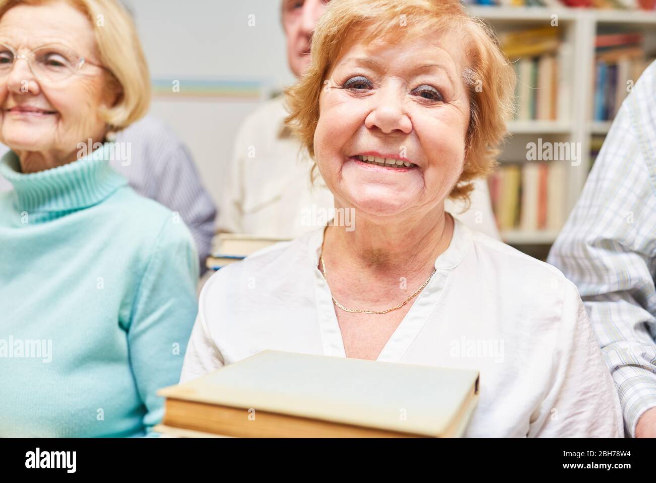 Donna anziana sorridente mentre prende in prestito libri in biblioteca nella casa di riposo Foto Stock