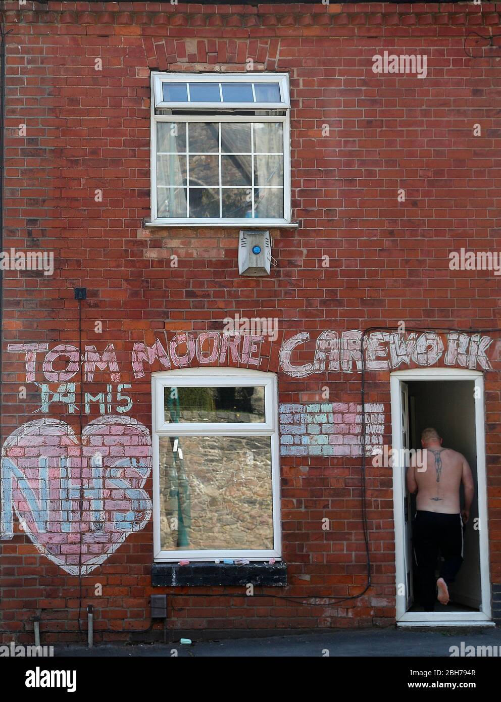 Anstey, Leicestershire, Regno Unito. 24 aprile 2020. Un uomo entra in una casa con un tributo al NHS e il capitano Tom Moore durante il blocco pandemico coronavirus. Credit Darren Staples/Alamy Live News. Foto Stock