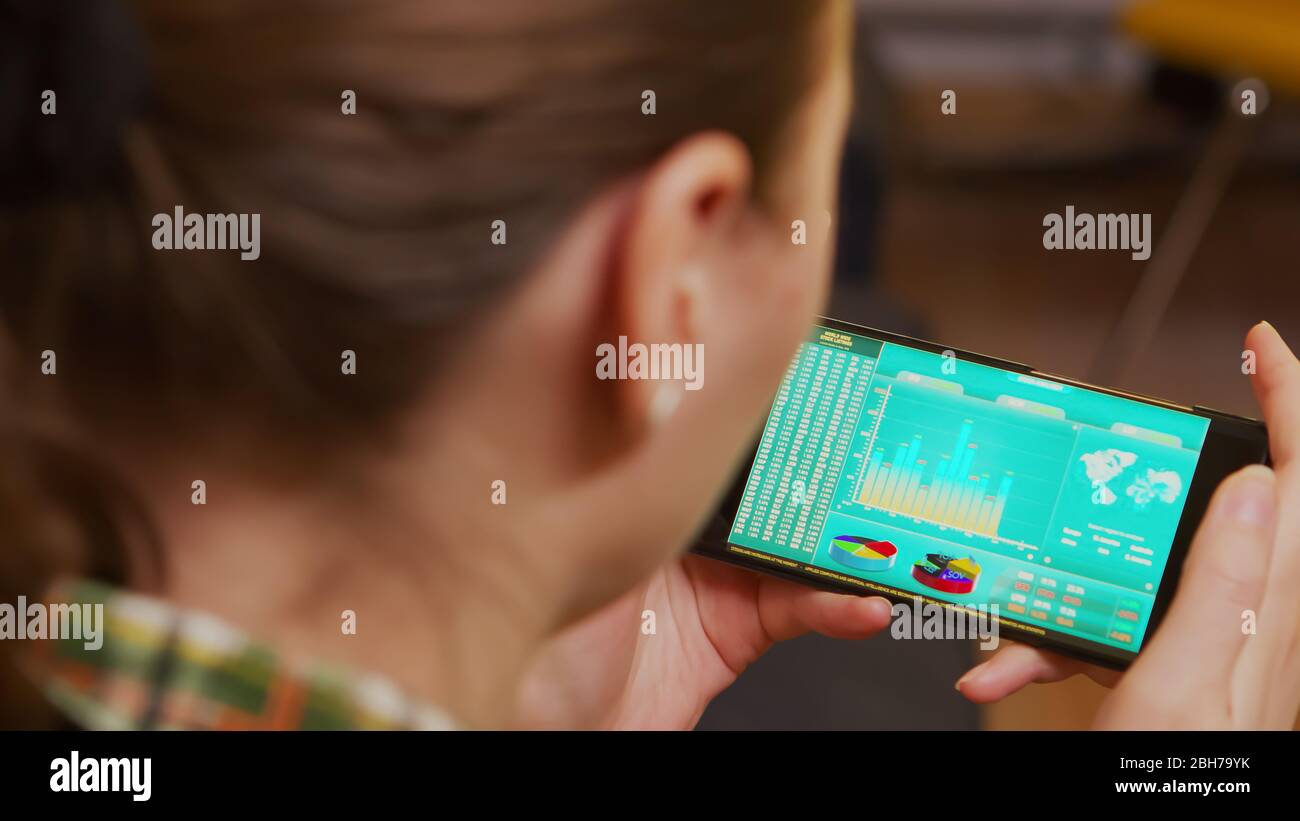 Retro della donna telefono con i grafici degli investimenti finanziari sul mercato azionario. Foto Stock