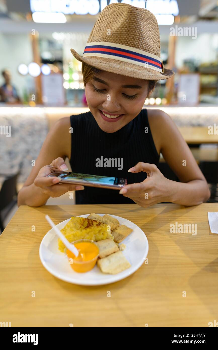Felice giovane turista asiatico donna che prende la foto del cibo con il telefono Foto Stock
