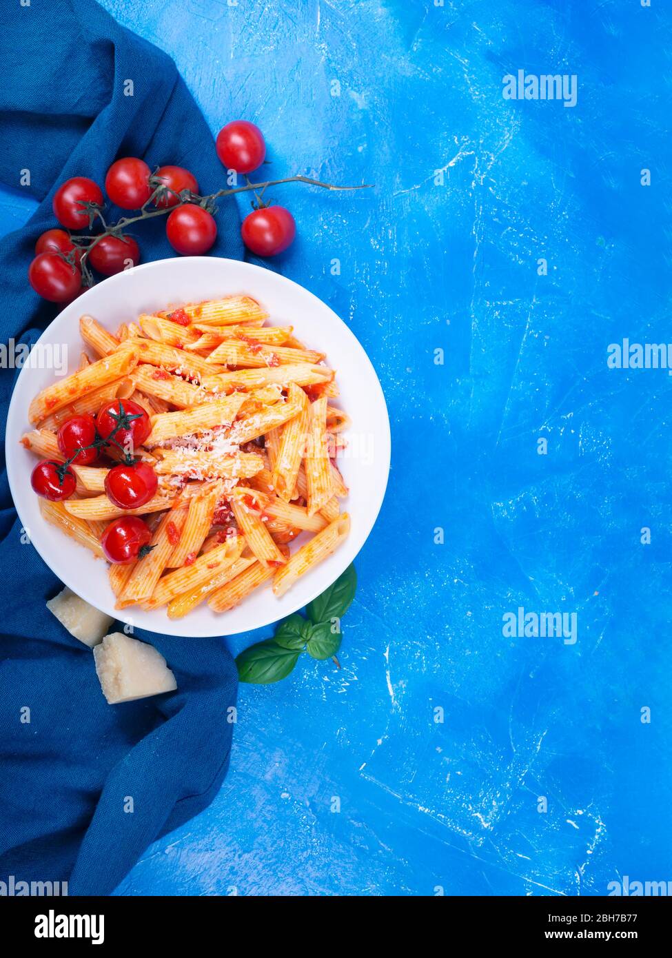 Pasta con salsa di pomodoro, basilico fresco, pomodori arrostiti e parmigiano su sfondo blu con vista laterale. Penne è un tipo estruso di pasta con il cil Foto Stock