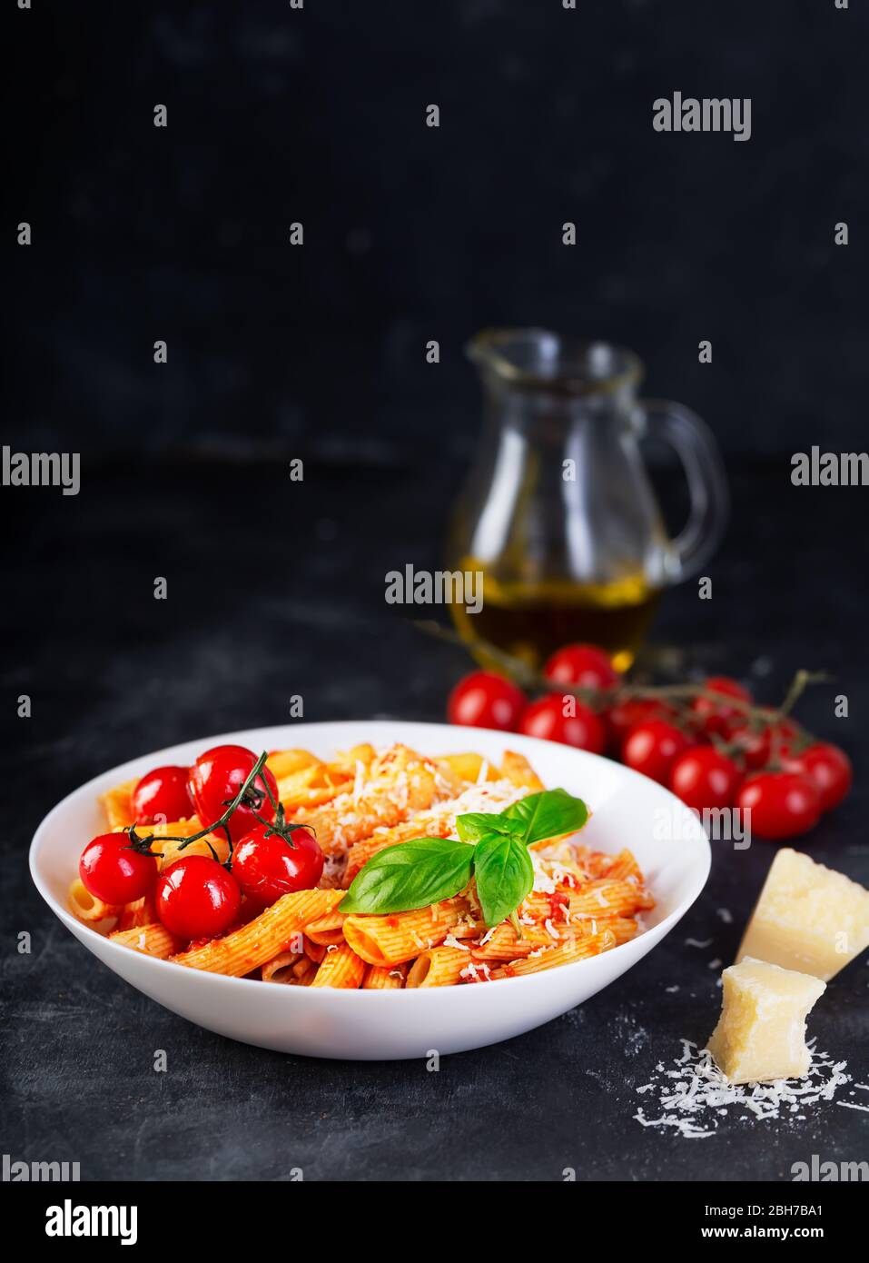 Pasta con salsa di pomodoro, basilico fresco, pomodori arrostiti e parmigiano su sfondo scuro con spazio per le copie. Penne è un tipo di pasta estrusa Foto Stock
