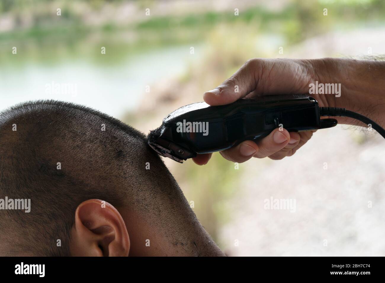 chiudi la mano dell'uomo con il regolacapelli per tagliare i capelli a casa durante il periodo di quarantena della malattia Foto Stock