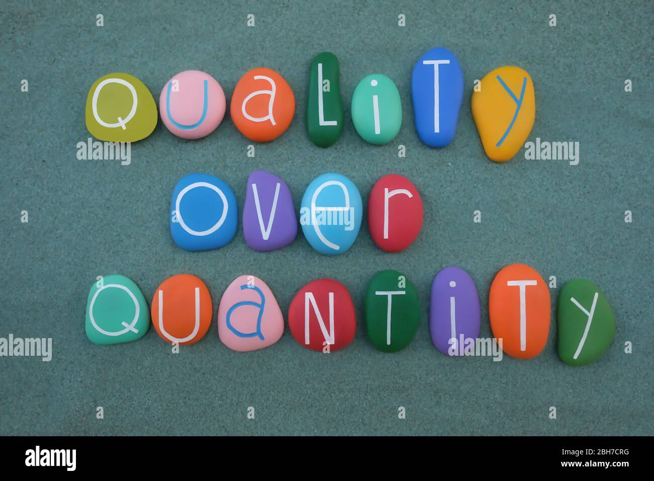 Qualità su quantità, frase concettuale composta da lettere di pietra multicolore su sabbia verde Foto Stock