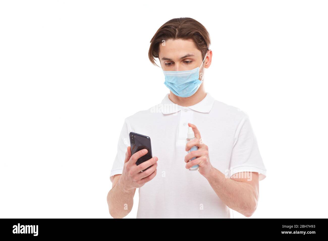 L'uomo europeo in maschera disinfetta il telefono. Foto concettuale sul tema della pandemia covid-2019. Isolato su sfondo bianco Foto Stock
