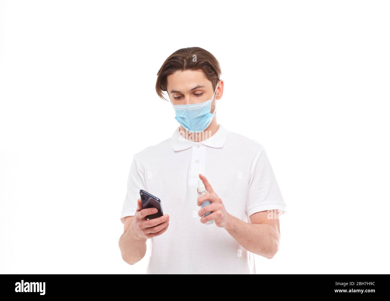 L'uomo europeo in maschera disinfetta il telefono. Foto concettuale sul tema della pandemia covid-2019. Isolato su sfondo bianco Foto Stock