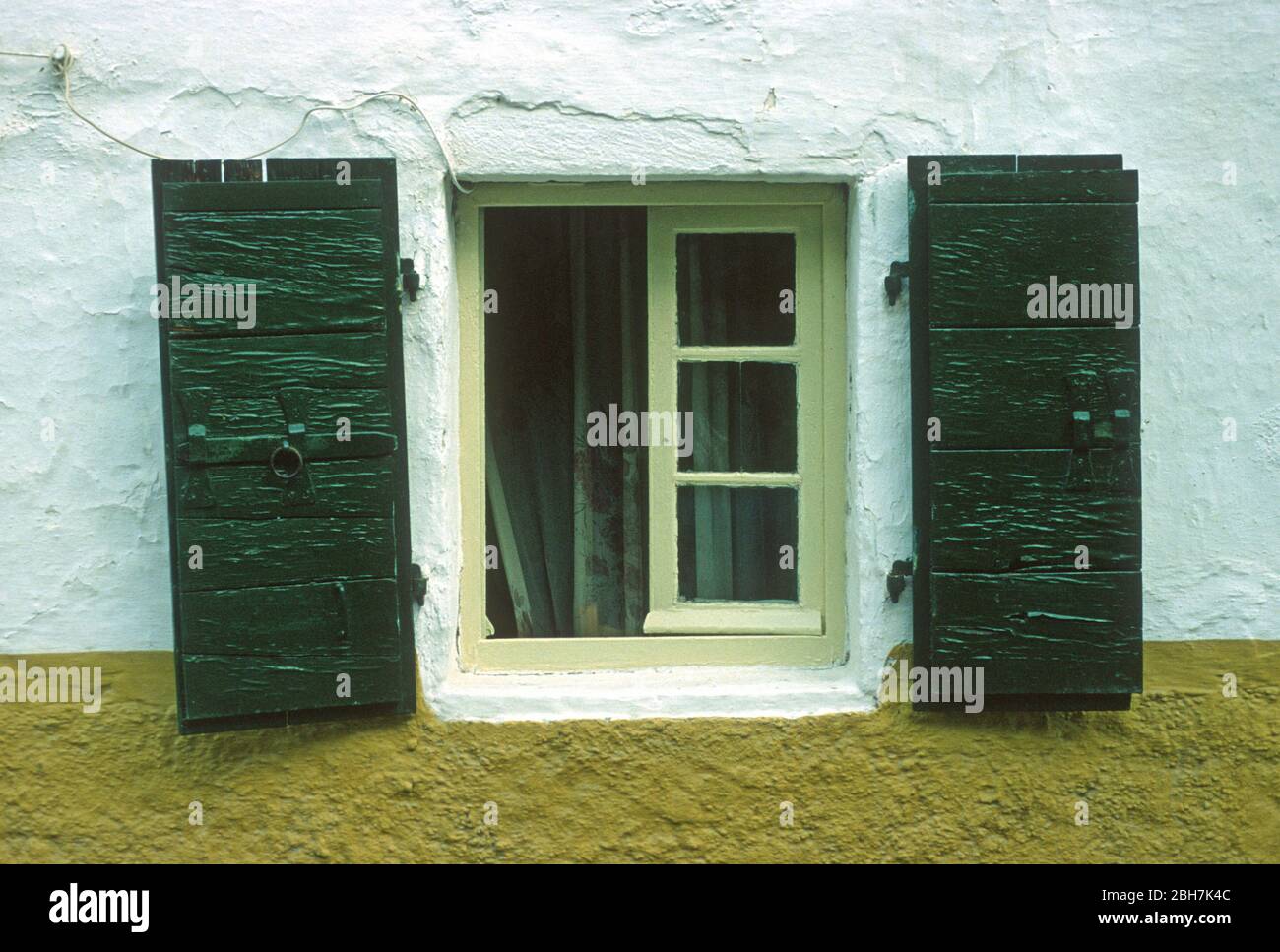 Verde scuro, persiane di legno ripiegate sul lato di una finestra di limone in un giallo e bianco, dipinto parete a Paxos, Grecia. Vedere l'altra immagine in cui gli otturatori sono chiusi. Foto Stock