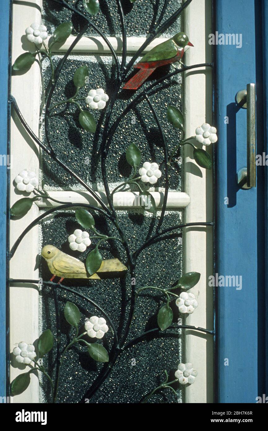 Griglia in metallo ornato con fiori, foglie e uccelli incatenati sopra i vetri di una casa blu e bianca una porta a Troodos, Cipro. Troodos, il Monte Olimpo, è stato dichiarato patrimonio dell'umanità dall'UNESCO. Foto Stock