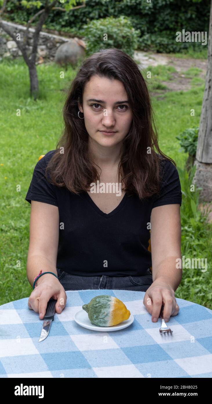 Giovane ragazza seduta ad un tavolo davanti ad un limone marcio. Spreco di cibo. Foto Stock