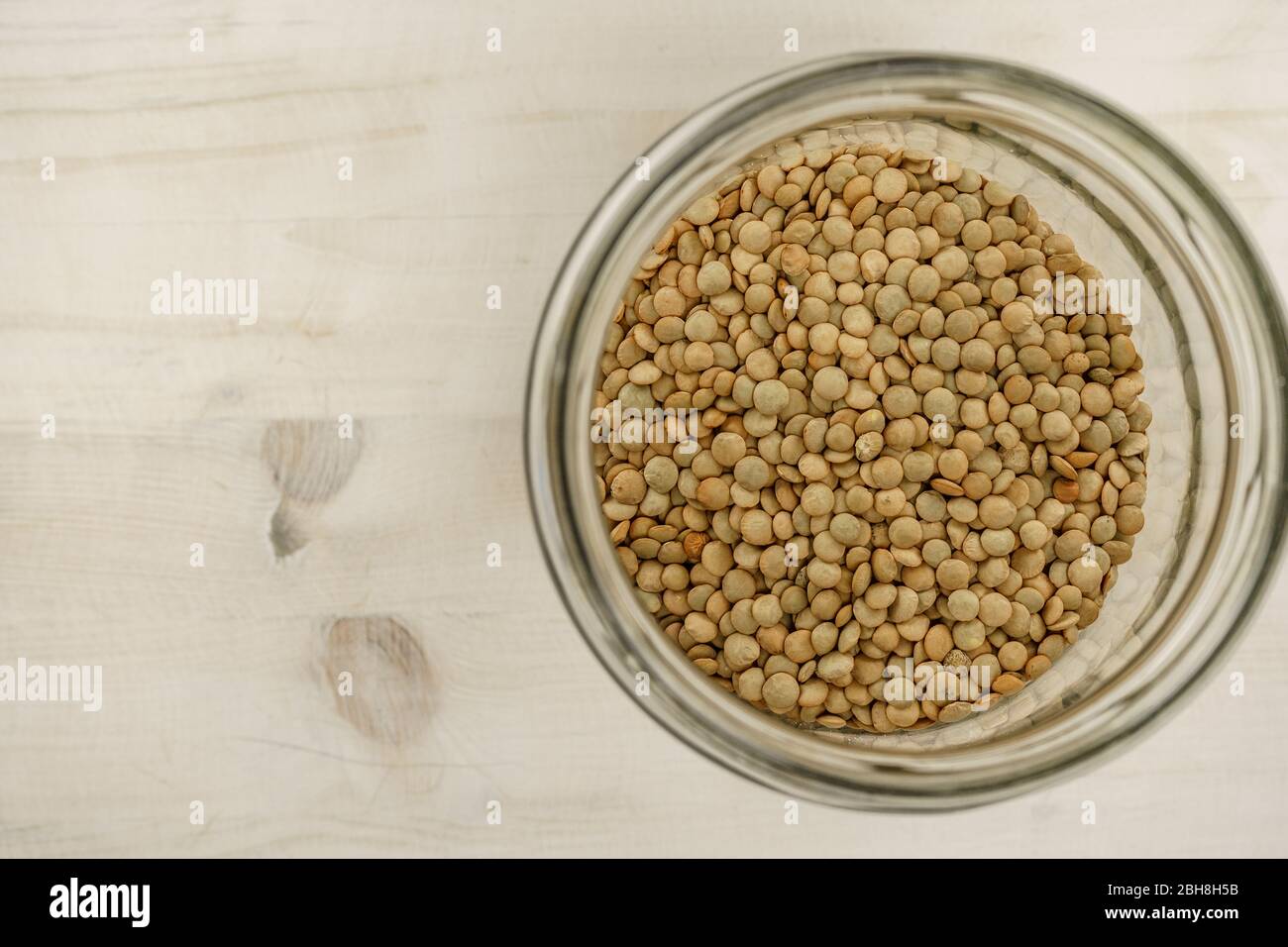 Torna al tema naturale dell'alimento vegano copy space: Dall'alto in basso piatto vista di un grande vaso di vetro riempito di lenticchie essiccate su sfondo tavolo di legno chiaro Foto Stock