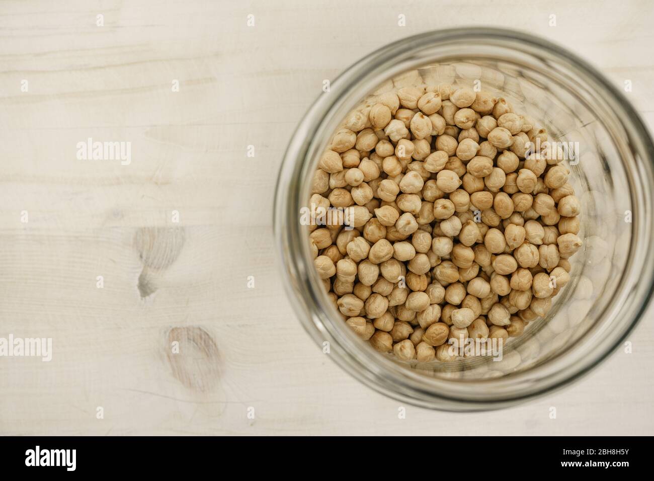 Torna al tema naturale dell'alimento vegano copy space: Dall'alto in basso piatto vista di un grande vaso di vetro riempito di ceci secchi su sfondo tavolo di legno chiaro Foto Stock