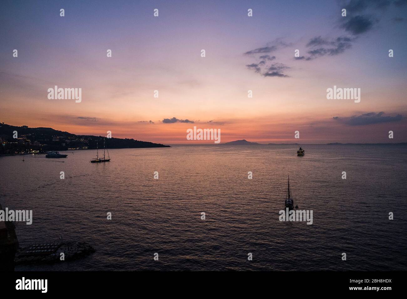 Viaggia e goditi la vita con molte barche nel mezzo del mare con isole sullo sfondo. Wanderlust con cielo rosa tramonto colorato e persone che viaggiano via per la prossima destinazione avventura Foto Stock