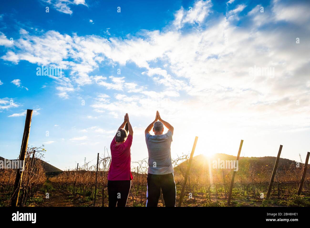 Yoga e meditazione posizione con due anziani uomo e donna insieme guardando e dando grazie al sole di mattina presto o tramonto d'oro - attività all'aperto sano per le persone lifestyle piacevole Foto Stock