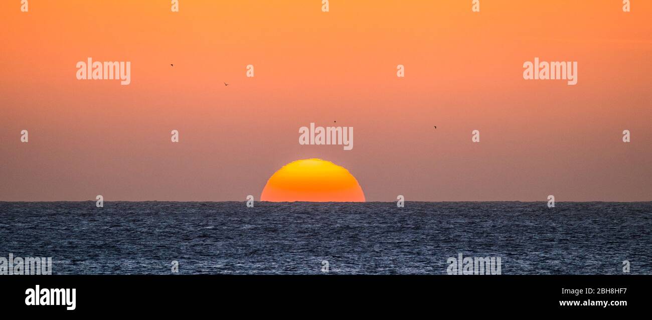 Tramonto o momento di alba sull'oceano con il sole che tocca la linea dell'orizzonte sull'acqua - romantico e turistico concetto per vacanza di viaggio sfondo colorato Foto Stock