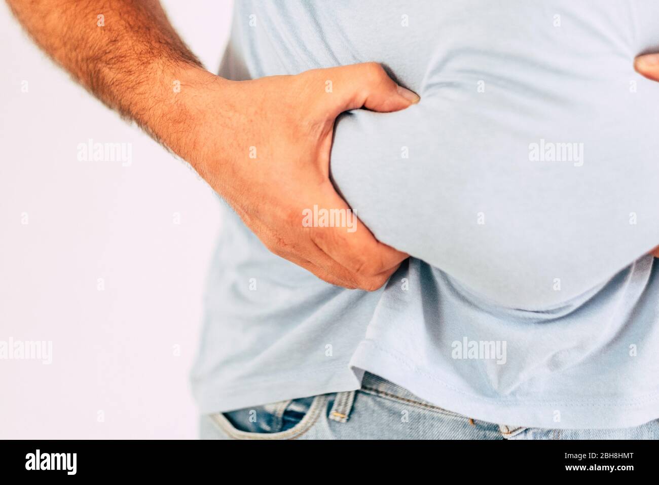Primo piano della mano dell'uomo caucasico che tiene il grasso addominale del ventre - concetto di alimento e dieta della roba di rifiuto, di benessere e di esercitazioni sportive per rimanere sano - esempio difettoso di lifestyle Foto Stock