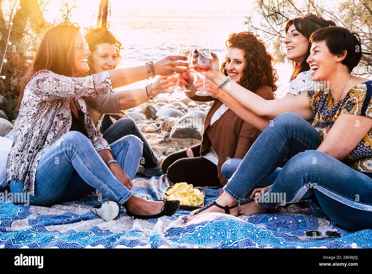 Gruppo di giovani allegre e felici donne godere e celebrare l'amicizia tostare con bicchieri da vino e sorridere insieme - luce soleggiata in background per il concetto di amicizia in spiaggia all'aperto Foto Stock