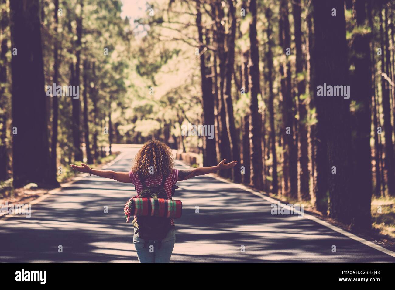 Eternità e successo soddisfazione vita concetto con la ragazza solitaria riccio hai rin il mezzo della strada lunga nella foresta con braccia aperte e zaino - wanderlust e viaggi stile persone Foto Stock