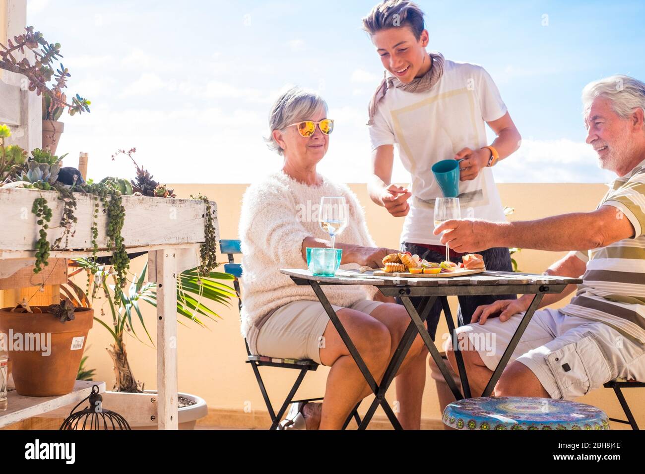 nonni adulti adulti e nipoti adolescenti. godetevi l'aria aperta in terrazza con cibo e bevande. vista sull'oceano e sulla città, vacanza giorno di sole bello clima concetto e sfondo. persone felici famiglia insieme Foto Stock